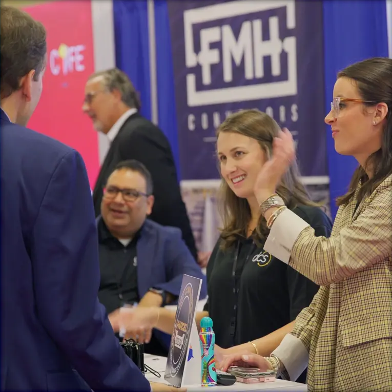 Attendees speak with exhibitors at a conference booth.