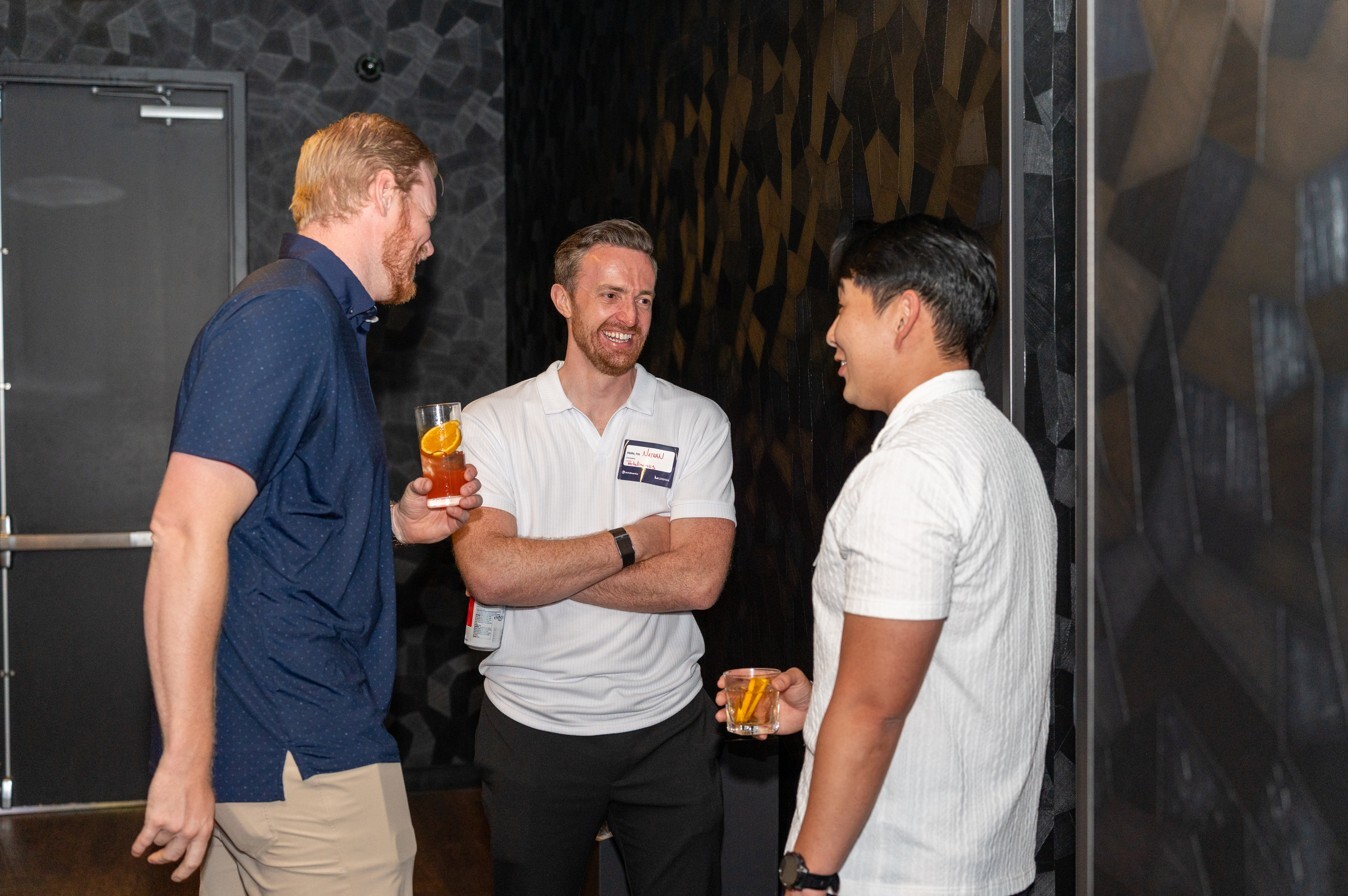 Three attendees converse during a networking event, with drinks in hand